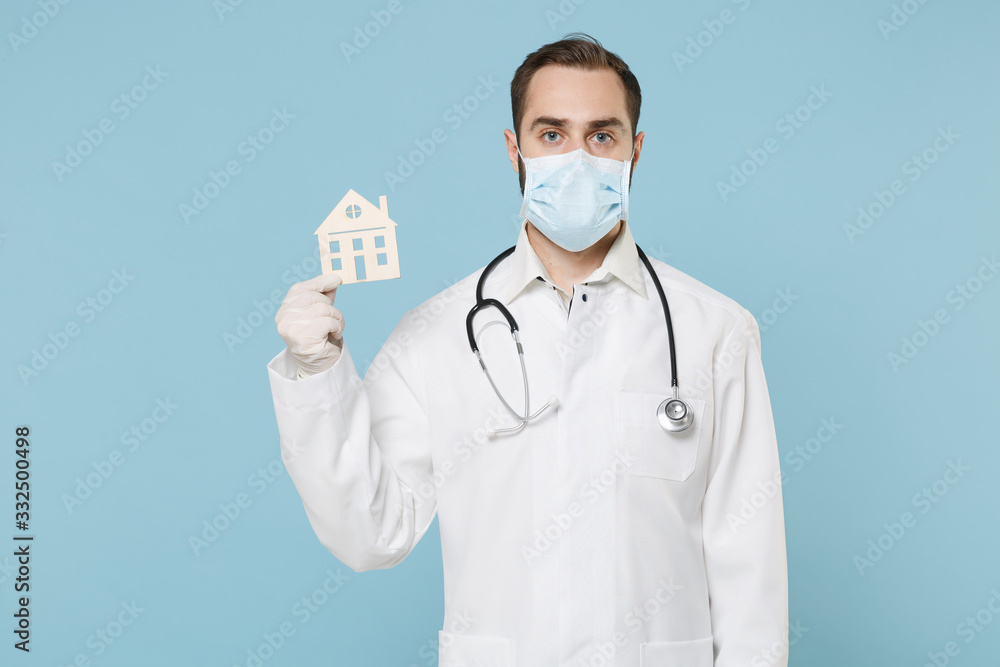 Male doctor man in medical gown sterile face mask gloves isolated on blue background. Epidemic pandemic coronavirus 2019-ncov sars covid-19 flu virus concept. Hold house, recommending staying home. Male doctor man in medical gown sterile face mask gloves isolated on blue background. Epidemic pandemic coronavirus 2019-ncov sars covid-19 flu virus concept. Hold house, recommending staying home.