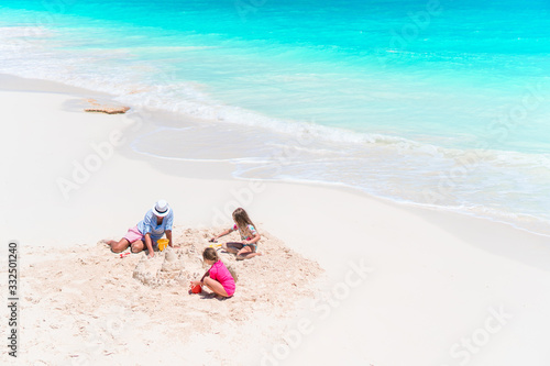 Father and little daughters making sand castle at tropical beach