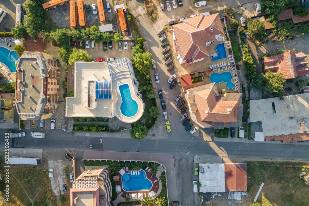 Top down aerial view of hotels roofs, streets with parked cars and swimming pools with blue water in resort city near the sea.