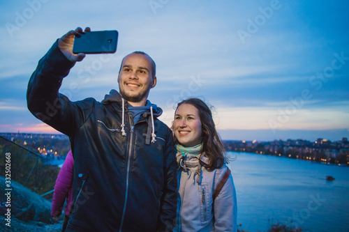 Young tourist couple taking a selfie at Skinnarviksberget on early evening in autumn. Beautiful Stockholm evening selfie from famous vantage point. photo