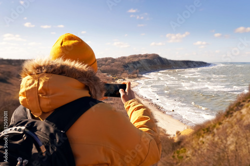 A man on a mountainside looks at the sea while traveling.