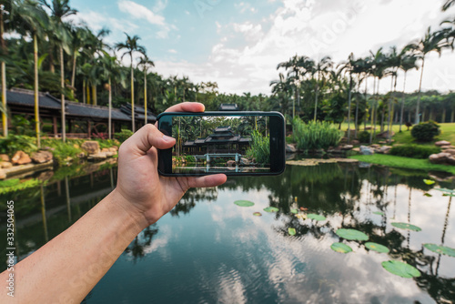 Crop hand using smartphone and taking photo of oriental building on tropical lake of Qingxiu Mountain, China photo