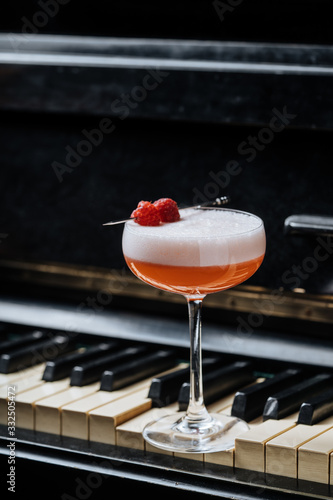 Red alcohol cocktail in stylish glass with white foam decorated with fresh raspberry on piano keys in restaurant photo