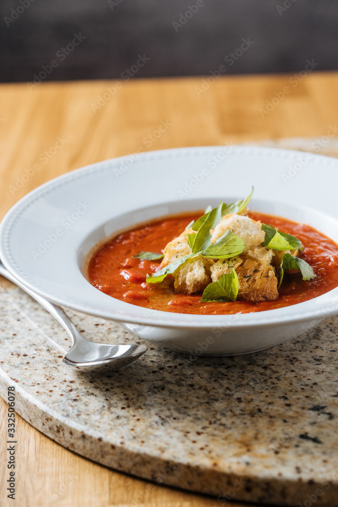 Red appetizing fresh tomato soup with greens on white plate on marble stand in cafe Red appetizing fresh tomato soup with greens on white plate on marble stand in cafe