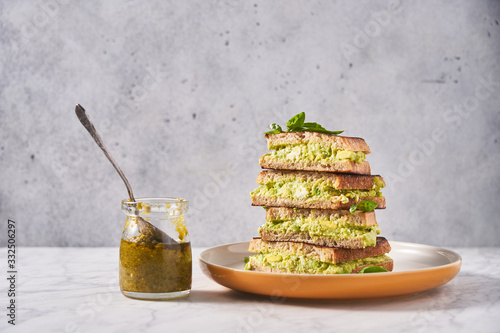Stack of rye bread sandwiches with avocado puree served with fresh mint on table with glass jar of pesto sauce  photo