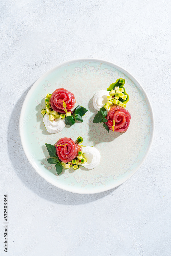 Salmon rolls with onion and herbs served on white ceramic plate on white table background Salmon rolls with onion and herbs served on white ceramic plate on white table background