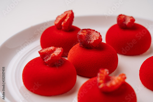 Closeup delectable cookies with vivid red icing and raspberries on top placed on white plate photo