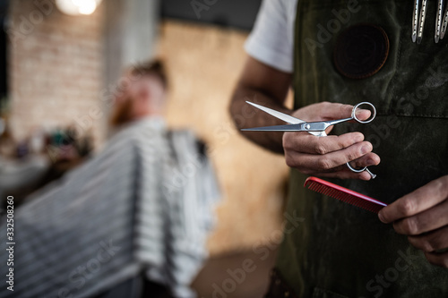 Unrecognizable crop man hairdresser holding scissors and comb in modern barbershop