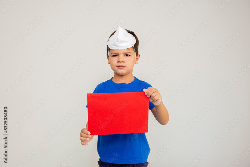 Caucasian boy with surgical mask on his head holding blank sheet. Face mask for protection against coronavirus outbreaks. Face mask against: virus, disease, epidemic, flu. COVID-19. Caucasian boy with surgical mask on his head holding blank sheet. Face mask for protection against coronavirus outbreaks. Face mask against: virus, disease, epidemic, flu. COVID-19.