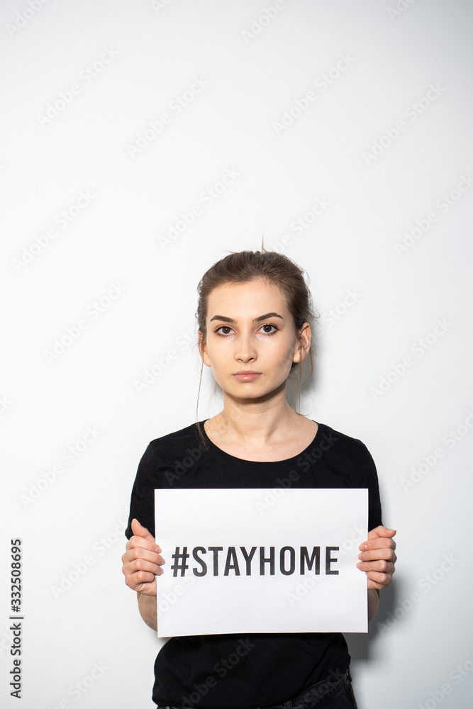 Girl holding a white paper with a text stay home Girl holding a white paper with a text stay home