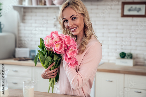 Cute charming girl with a bouquet of tulip flowers presented by her daughter in the kitchen