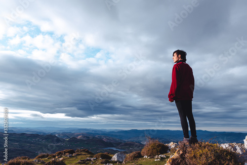 hiker standing and enjoying freedom viewing majestic scenery of countryside located along river shore in valley against foggy ridges at horizon under cloudy sky in Spain photo