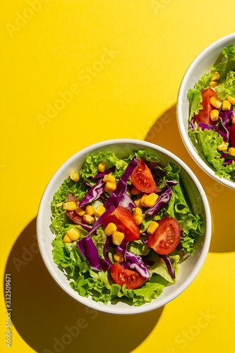 Fresh lettuce salad with Cherries tomatoes, red onion and corn, sunlight on pink background from above. Healthy food. Vegan food. photo