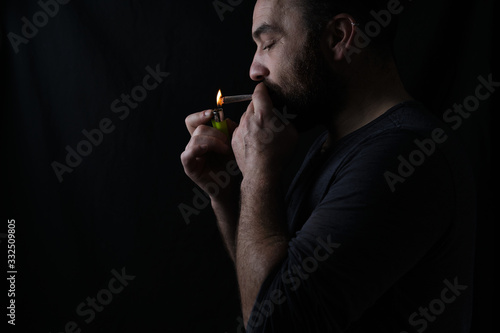 Side view of crop concentrated male smoker lighting up marijuana blunt on black background