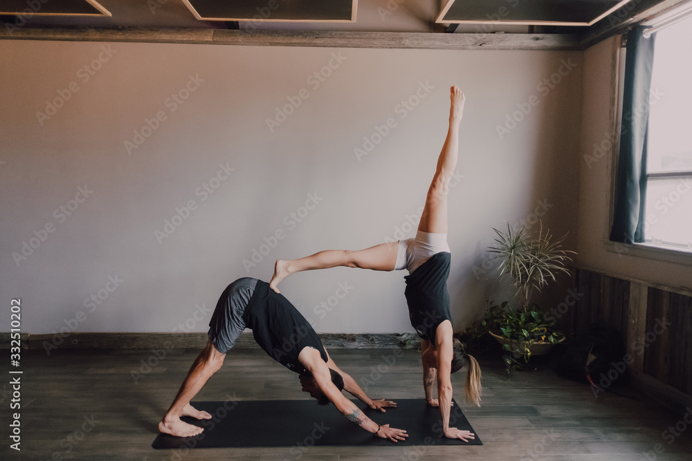 Side view of young barefooted man and focused woman in sportswear doing balance exercise standing in dog pose while training together on floor in light contemporary workout room Side view of young barefooted man and focused woman in sportswear doing balance exercise standing in dog pose while training together on floor in light contemporary workout room