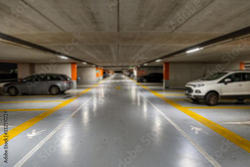 Yellow markings with blurred modern cars parked inside closed underground parking lot. © bilanol
