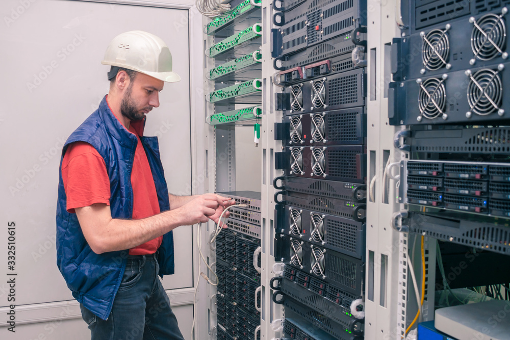 An engineer in a white helmet connects Internet wires to new equipment ...