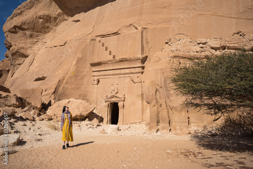 Happy woman traveler standing near tombs carved into cliffs in Madain Saleh in Saudi Arabia photo