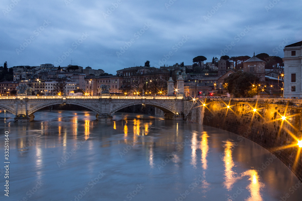Tiber river bridge at night with light set and Rome view on background. Long exposure in Italy on cloudy day. Top view.