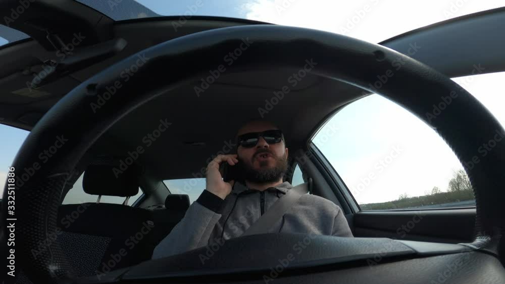 Adult man in hoodie driving car on highway and talking on phone, wide angle view through the steering wheel Adult man in hoodie driving car on highway and talking on phone, wide angle view through the steering wheel