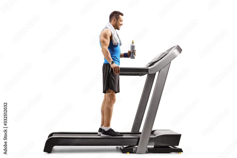 Fit man standing on a treadmill with a bottle of isotonic drink Fit man standing on a treadmill with a bottle of isotonic drink