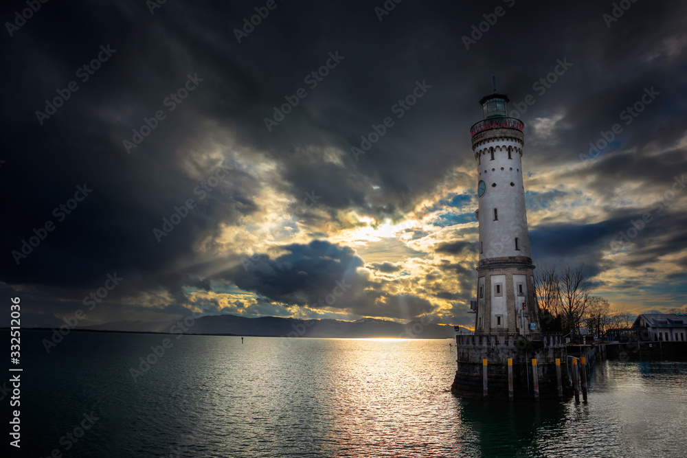 Lighthouse in port of Lindau town by the bodensee lake in Germany with dark clouds and Alp mountains in the background Lighthouse in port of Lindau town by the bodensee lake in Germany with dark clouds and Alp mountains in the background