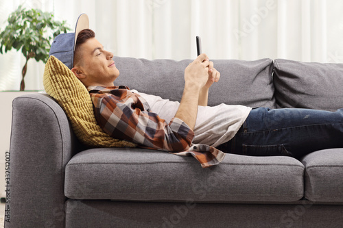 Young guy lying on a sofa and looking at a mobile phone