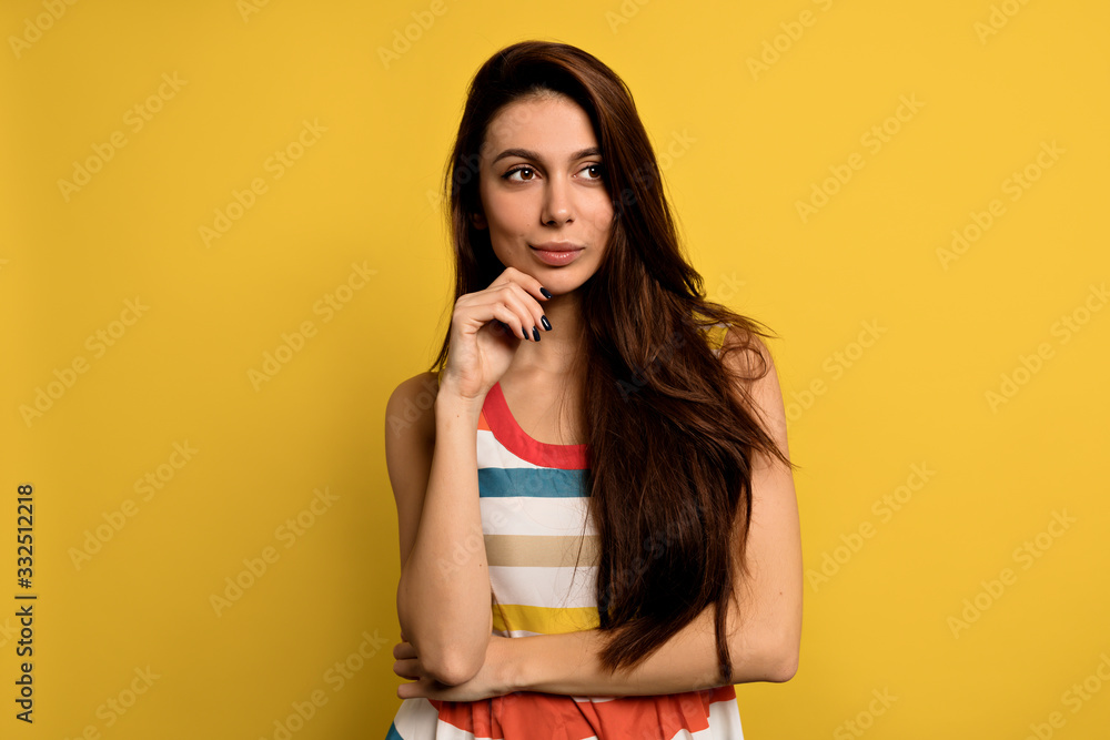 Fototapeta premium Stunning female model posing with face expression on yellow background. Close-up portrait of stylish european girl standing with playful look in front of wall