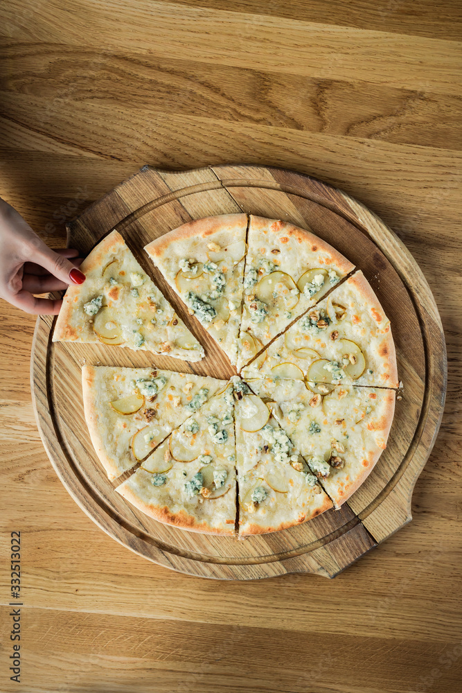 A woman's hand stealing a slice of pizza from a wooden round board, top view photo