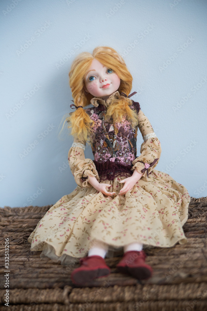 Hand made doll in a colored dress with long hair sitting on a brown chest