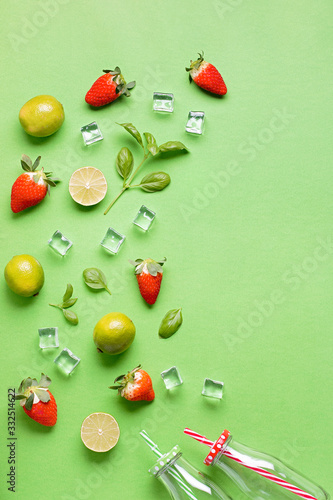 Flat lay with ingredients for summer refreshing drink or smoothie, ice cubes, herbs and glass jars on green background, top view. Strawberry, lime, ice and basil for delicious summer cocktail