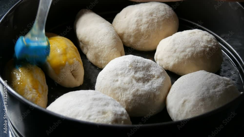 Homemade baking on a baking sheet, a female baker greases the balls from the dough with egg yolk. Special kitchen silicone brush for greasing dough. Ukrainian domestic dumplings. Homemade baking on a baking sheet, a female baker greases the balls from the dough with egg yolk. Special kitchen silicone brush for greasing dough. Ukrainian domestic dumplings.