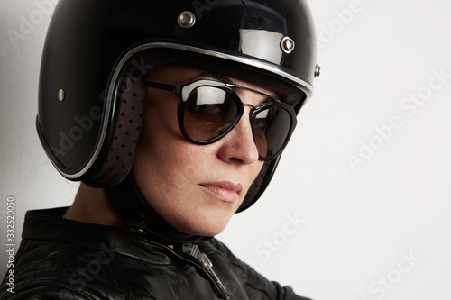 Close-up of attractive biker woman posing on the white wall and wearing black shiny helmet. © face_reader_img