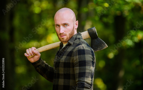 Man checkered shirt use axe. Brutal male in forest. Power and strength. Lumberjack carry ax. Bald woodsman. Harvest firewood. Hike vacation. Hike in forest. Forest care. Determination of human spirit
