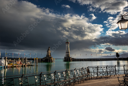 Lighthouse and lion monument in port of Lindau town by the bodensee lake in Germany. Dark clouds and Alps mountains in the background. © Milan