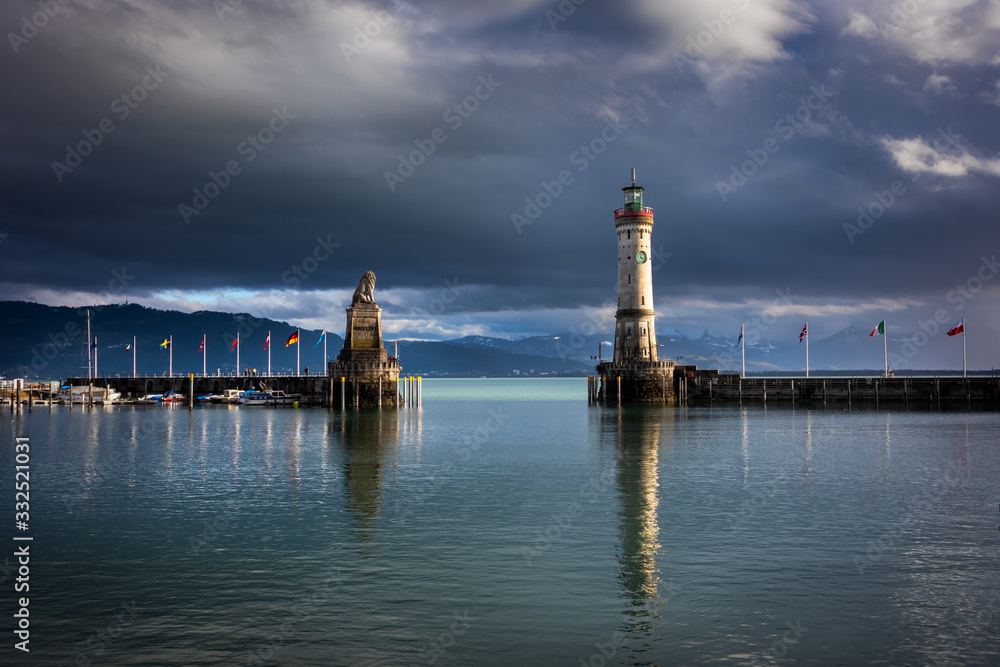 Lighthouse and lion monument in port of Lindau town by the bodensee lake in Germany. Dark clouds and Alps mountains in the background.