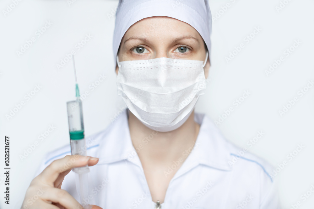 Female doctor in medical protective mask with a syringe close-up.