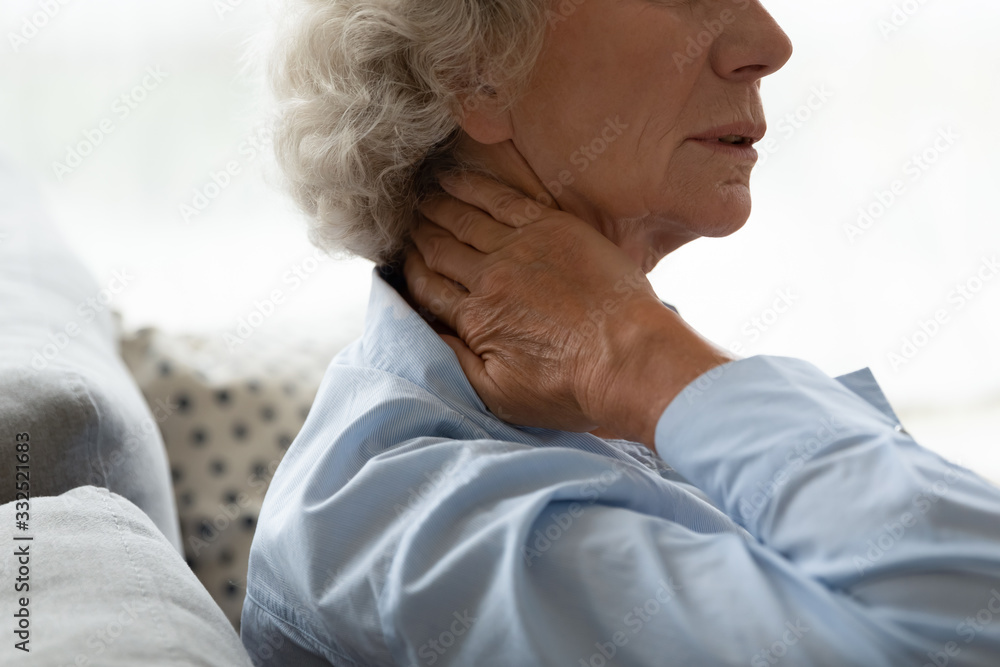 Hurt old female sit on couch touch neck suffer from painful spinal feeling sudden spasm, sick