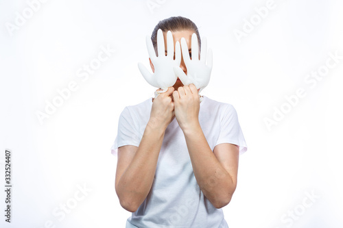 The girl holds white medical gloves in her hands. Protection against germs and the virus. She is in a white T-shirt on a white background.