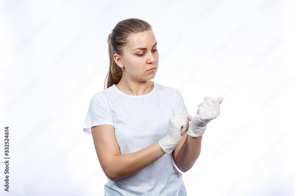 Girl paramedic puts on white medical gloves on hands. Protection against germs and viruses. She is in a white T-shirt on a white background. Girl paramedic puts on white medical gloves on hands. Protection against germs and viruses. She is in a white T-shirt on a white background.