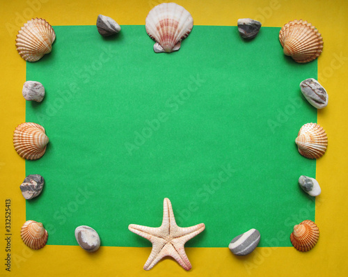The frame made of sea shells, pebbles and starfish on yellow and green background. Summer flat lay. Travel and vacation concept. Top view with copy space for your text
