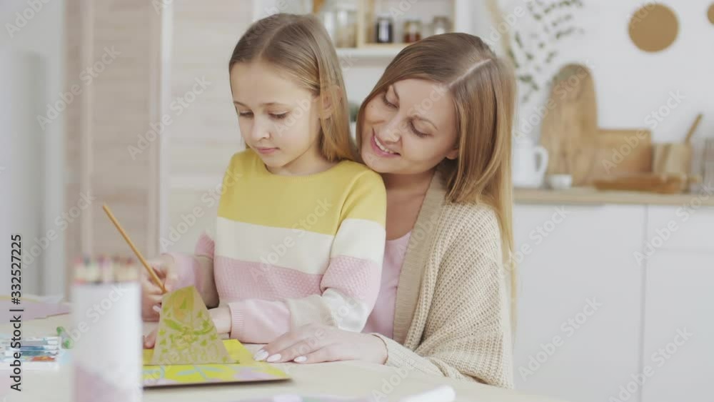 Medium shot of cheerful Caucasian woman spending time with her little daughter. They drawing together Medium shot of cheerful Caucasian woman spending time with her little daughter. They drawing together