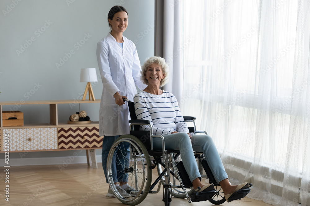 Portrait of young female nurse or caregiver posing give help to disabled happy old lady sitting in wheelchair, woman doctor assist support handicapped optimistic positive senior patient Portrait of young female nurse or caregiver posing give help to disabled happy old lady sitting in wheelchair, woman doctor assist support handicapped optimistic positive senior patient