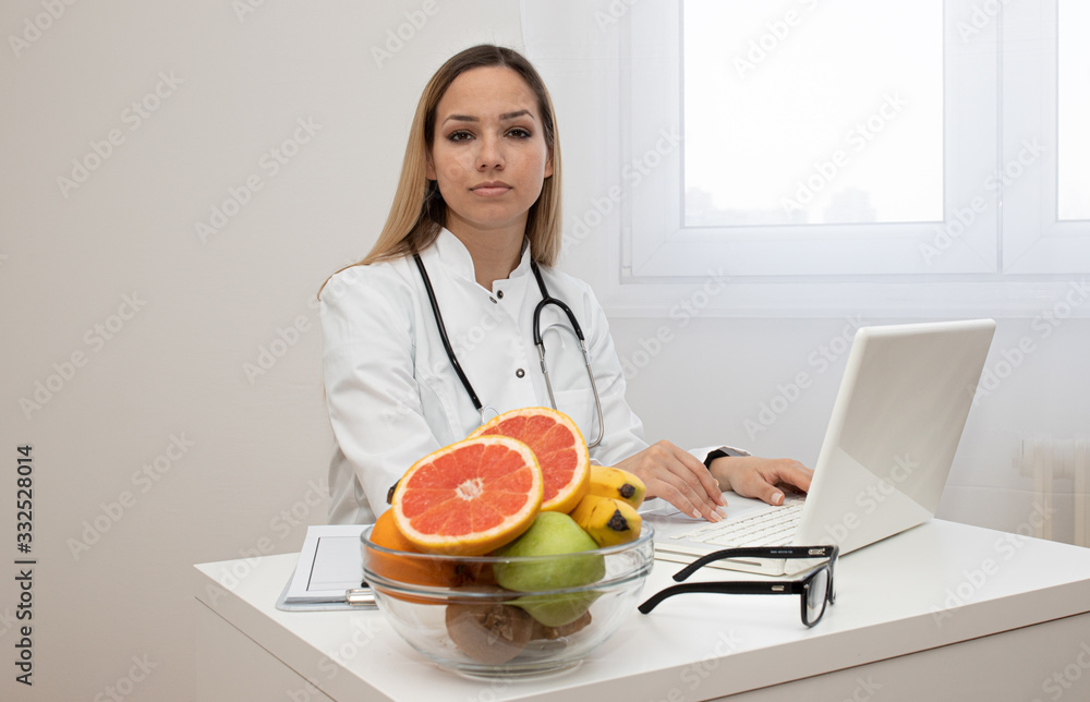 Female nutritionist with fruits working at her desk. Smiling nutritionist in her office, she is showing healthy vegetables and fruits, healthcare and diet concept. Female nutritionist with fruits working at her desk. Smiling nutritionist in her office, she is showing healthy vegetables and fruits, healthcare and diet concept.