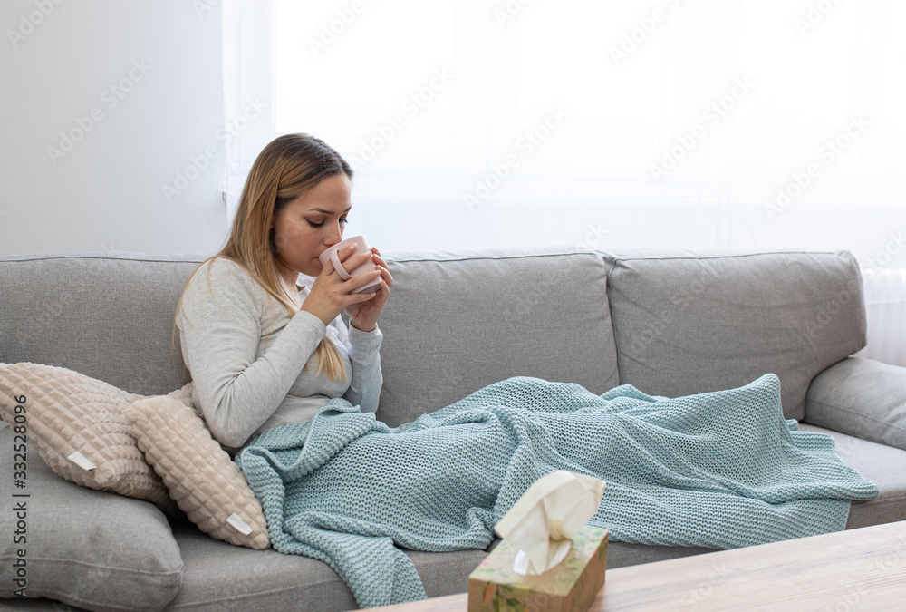 Sick woman sitting under the blanket. Sick woman with seasonal infections, flu, allergy lying in bed. Sick woman covered with a blanket lying in bed with high fever and a flu, resting and drinking tea