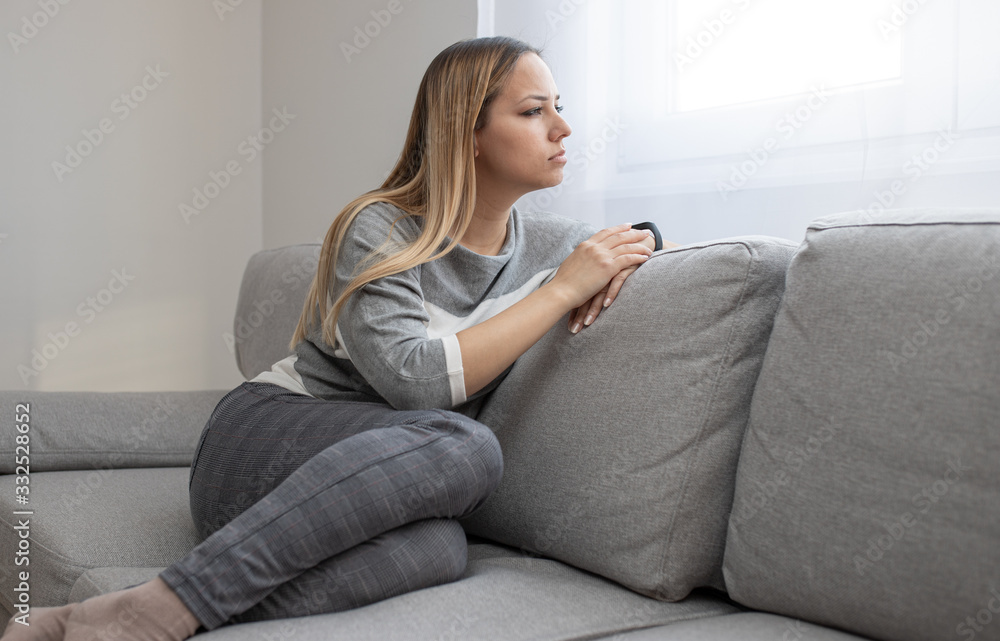 Sad and depressed woman sitting on sofa and looking at distance. Woman bored at home. Sad and depressed woman sitting on sofa and looking at distance. Woman bored at home.
