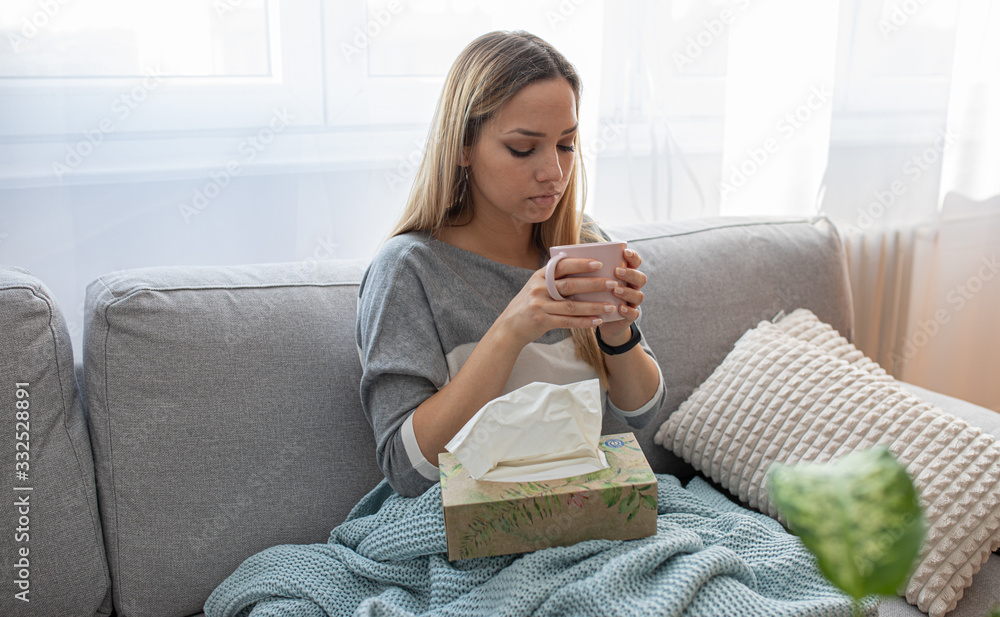 Sick woman sitting under the blanket. Sick woman with seasonal infections, flu, allergy lying in bed. Sick woman covered with a blanket lying in bed with high fever and a flu, resting and drinking tea Sick woman sitting under the blanket. Sick woman with seasonal infections, flu, allergy lying in bed. Sick woman covered with a blanket lying in bed with high fever and a flu, resting and drinking tea