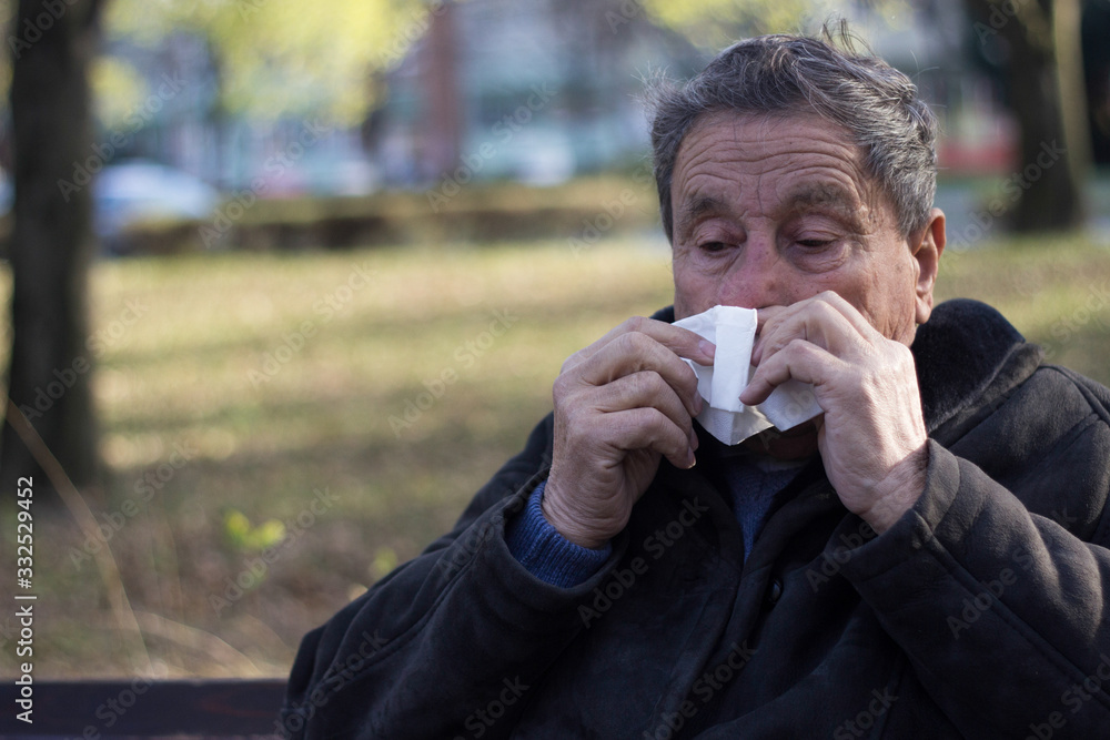 Portrait of a coughing senior man outdoors, looking down. Senior man having sickness, allergies Portrait of a coughing senior man outdoors, looking down. Senior man having sickness, allergies