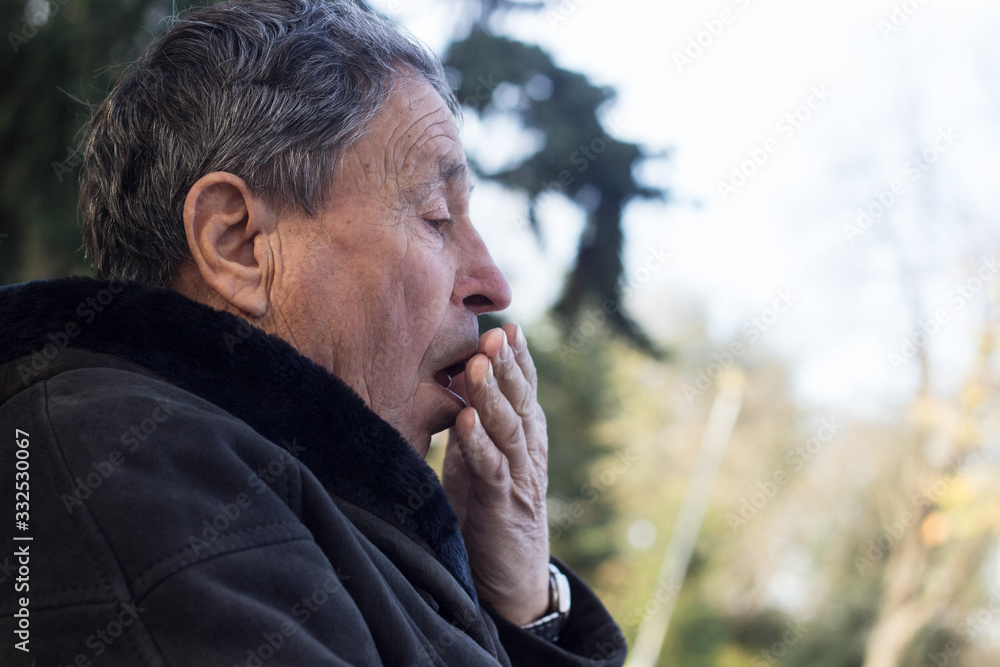 Portrait of a coughing senior man outdoors, looking down. Senior man having sickness, allergies Portrait of a coughing senior man outdoors, looking down. Senior man having sickness, allergies