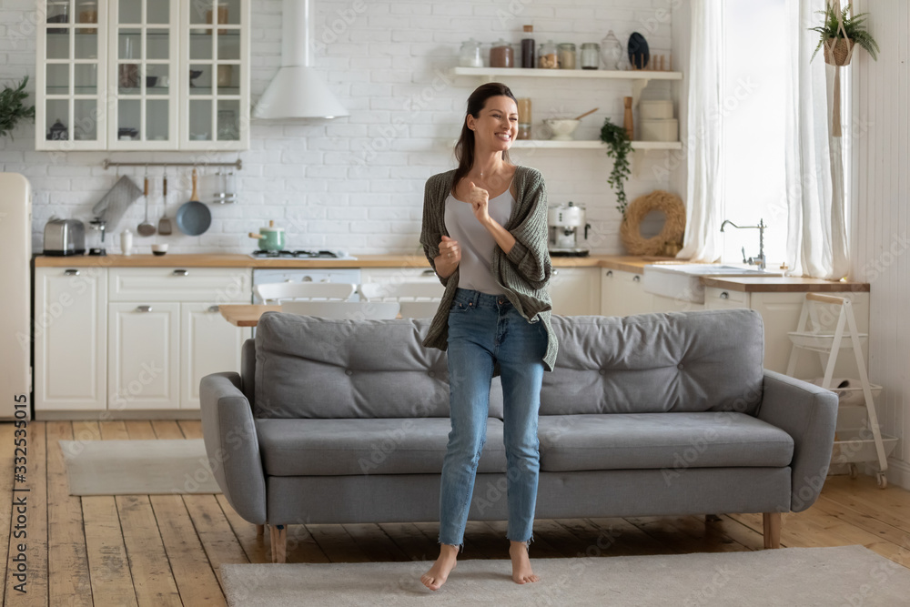 Obraz premium Overjoyed young woman enjoy free leisure weekend at home dancing listen to music in living room, smiling happy millennial female have fun moving to rhythm being active in modern studio home